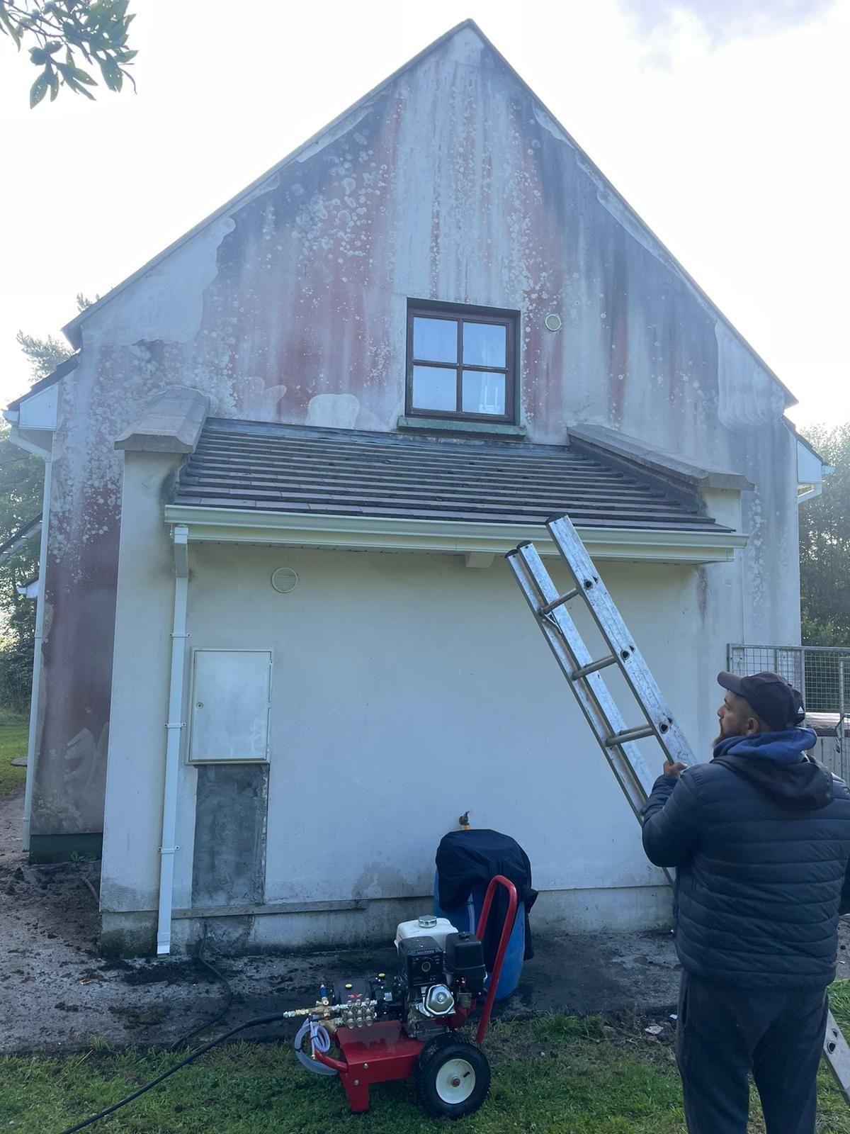 A man is standing in front of a white building with a ladder.
