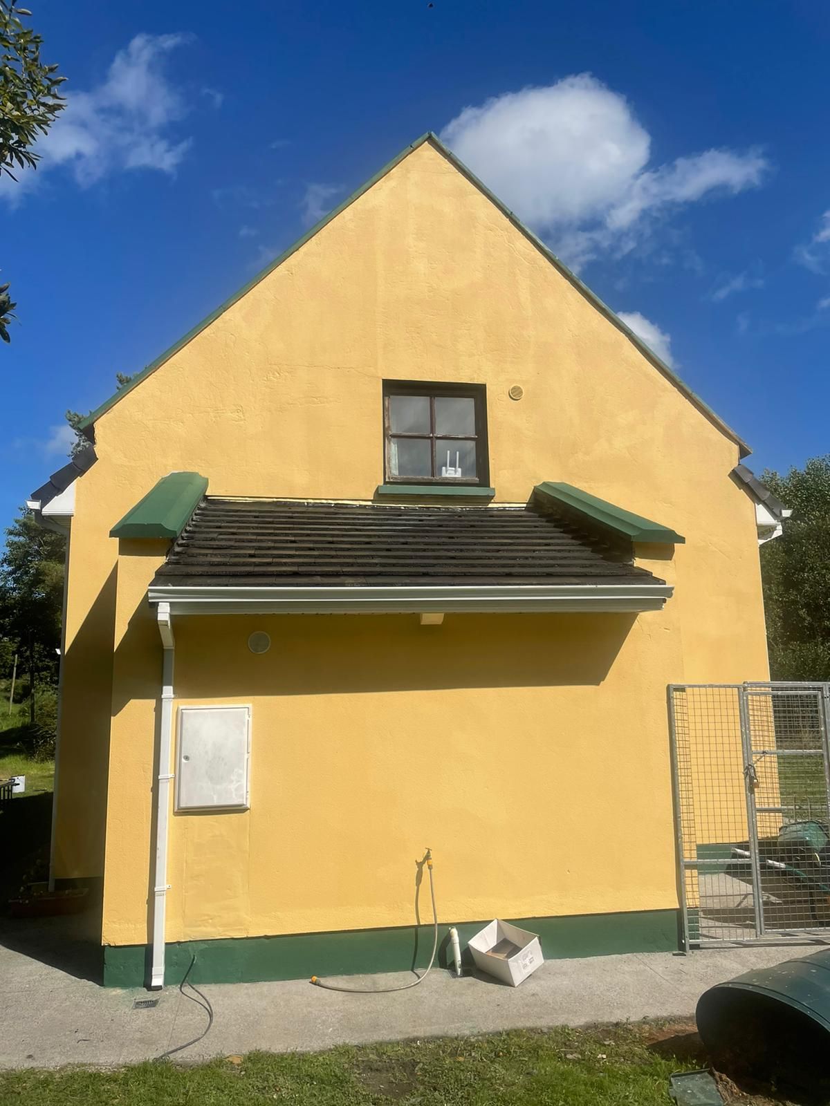 A yellow house with a green roof and a window.