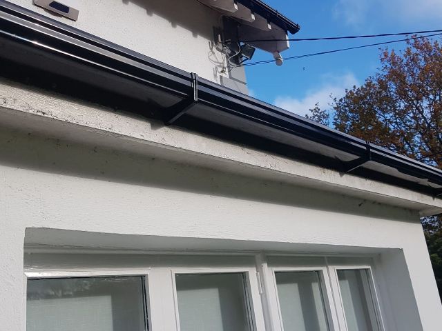 A white house with a black gutter on the roof.