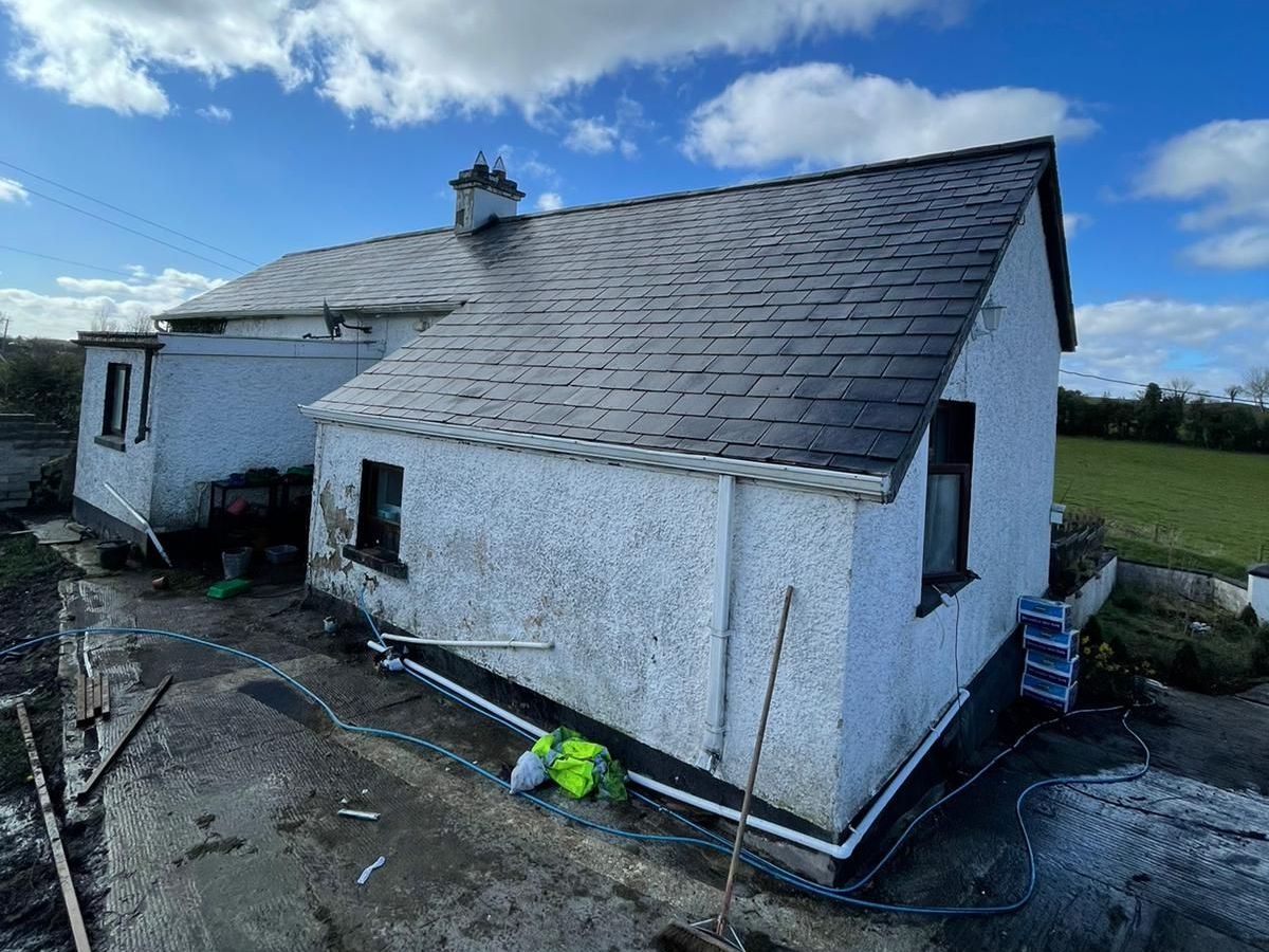 A white house with a slate roof is sitting in the middle of a field.