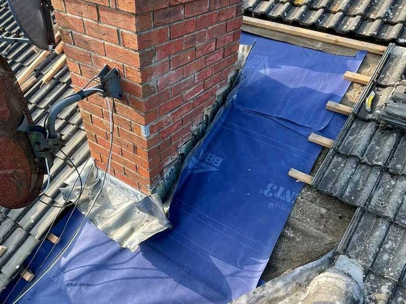 A brick chimney is sitting on top of a tiled roof.