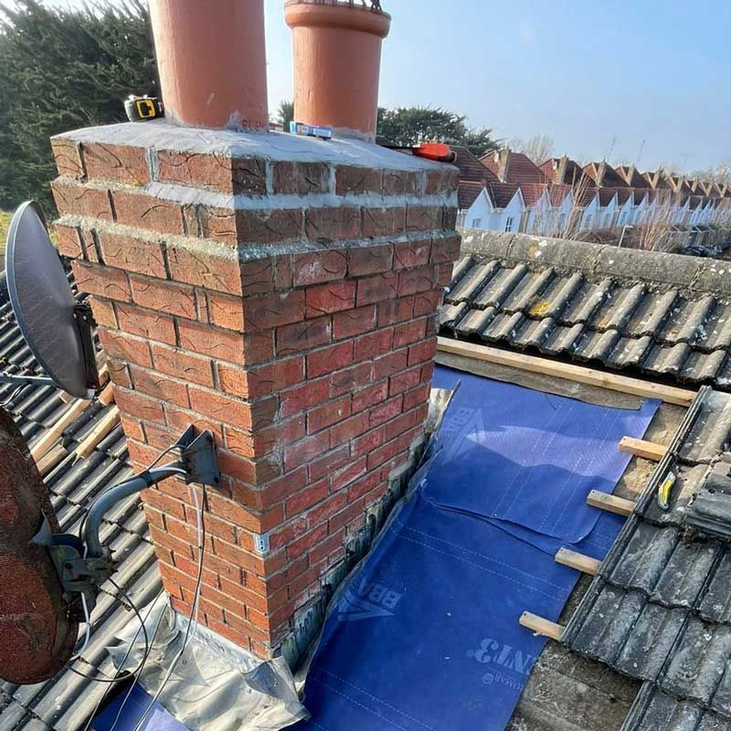 A brick chimney is sitting on top of a tiled roof.
