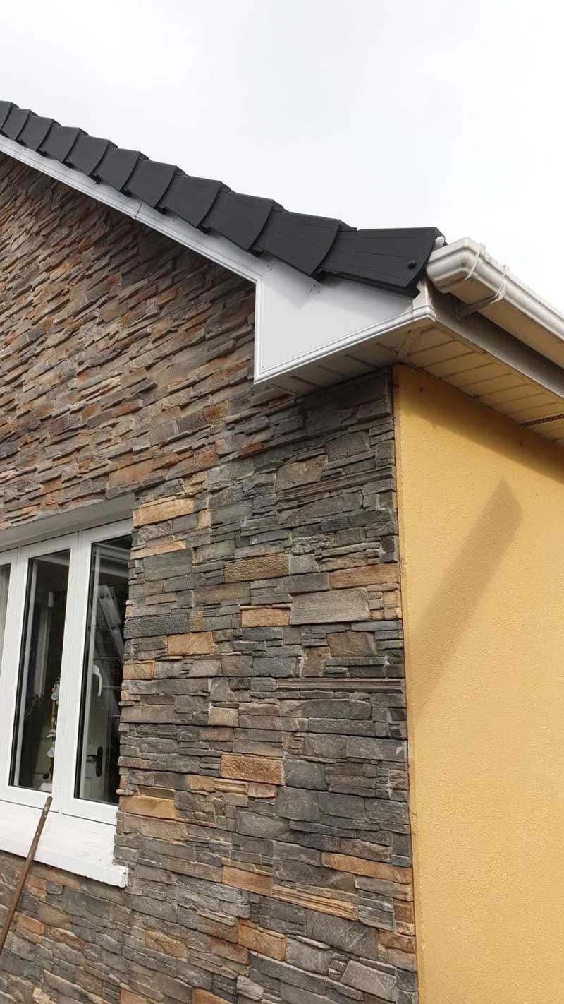 The side of a house with a stone wall and a window.
