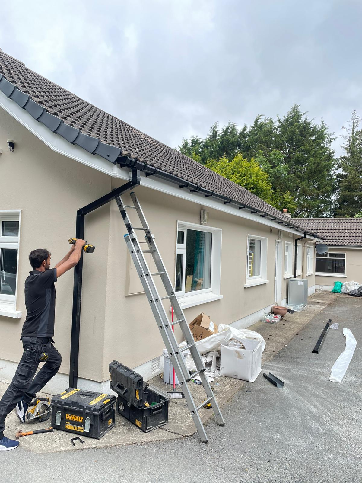 A man is installing a gutter on the side of a house.
