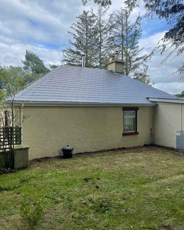 A small house with a gray roof and a large lawn in front of it.