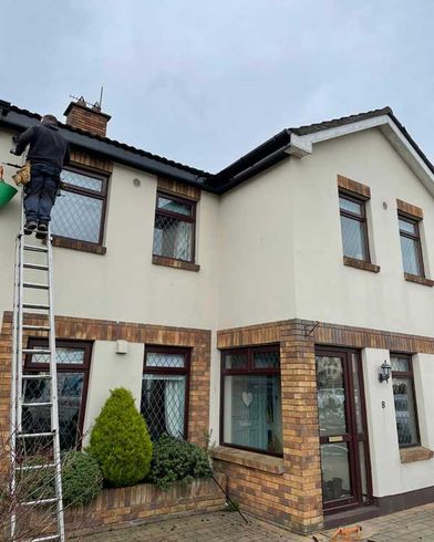 A man on a ladder is painting the side of a house.