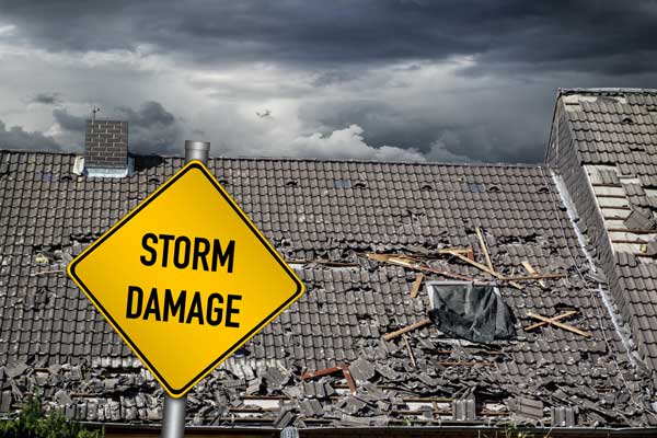A yellow sign that says `` storm damage '' is in front of a damaged roof.