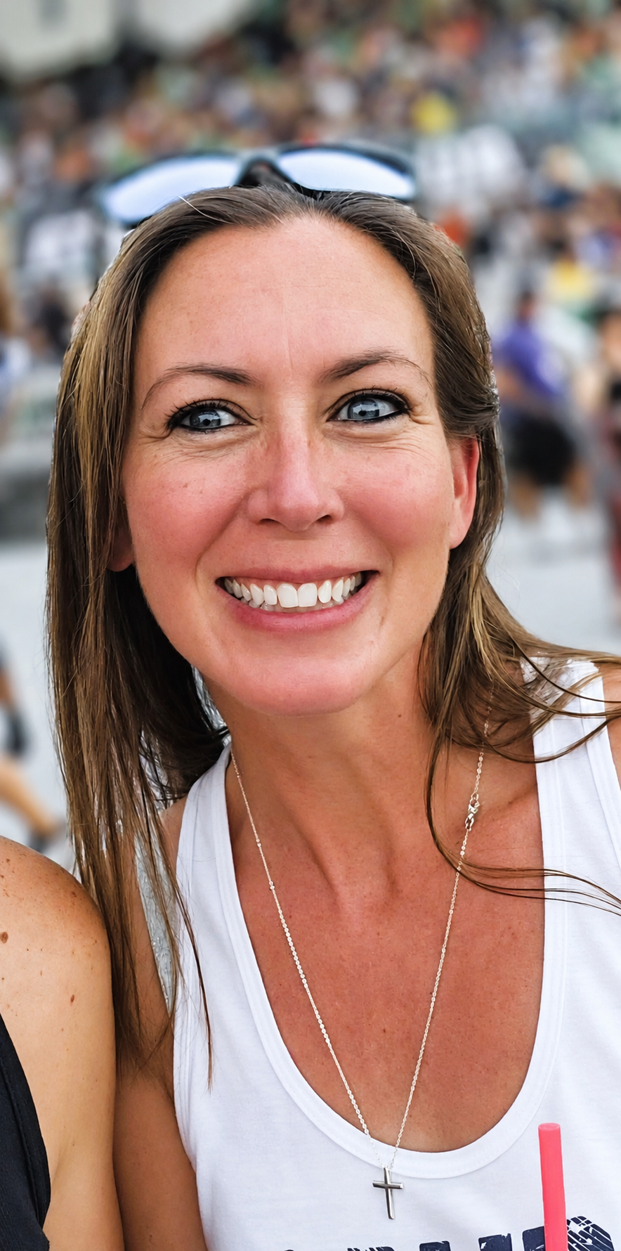 Smiling woman in a white top with sunglasses on her head at an outdoor event