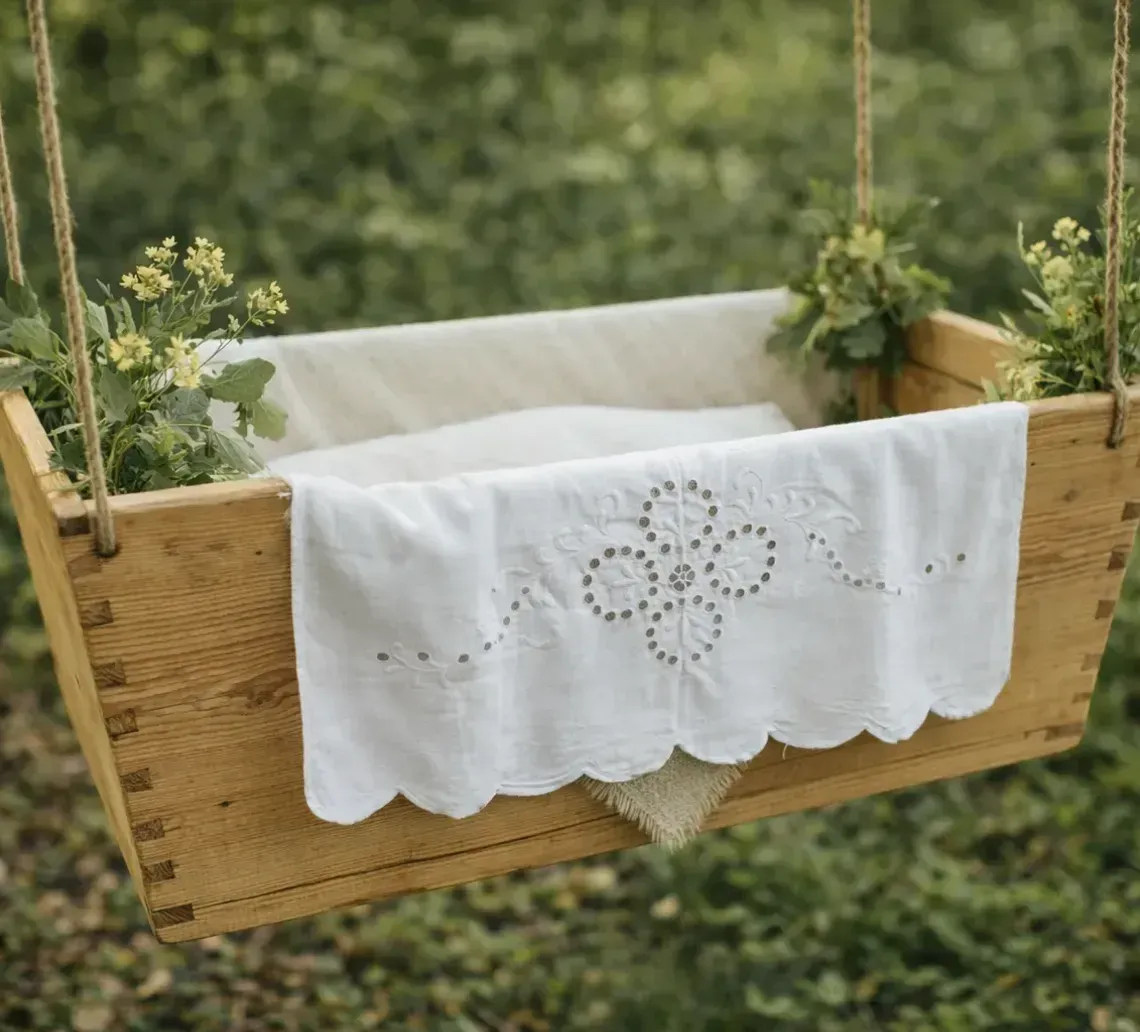 A wooden box swing hanging over a grassy field, decorated with white lace fabric and small yellow wildflowers.