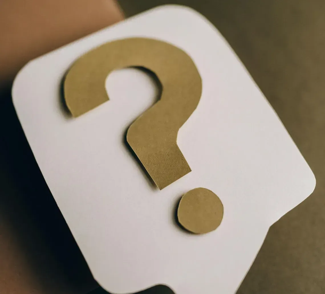 A gold-colored question mark cutout centered on a white, speech bubble-shaped tag against a dark background.