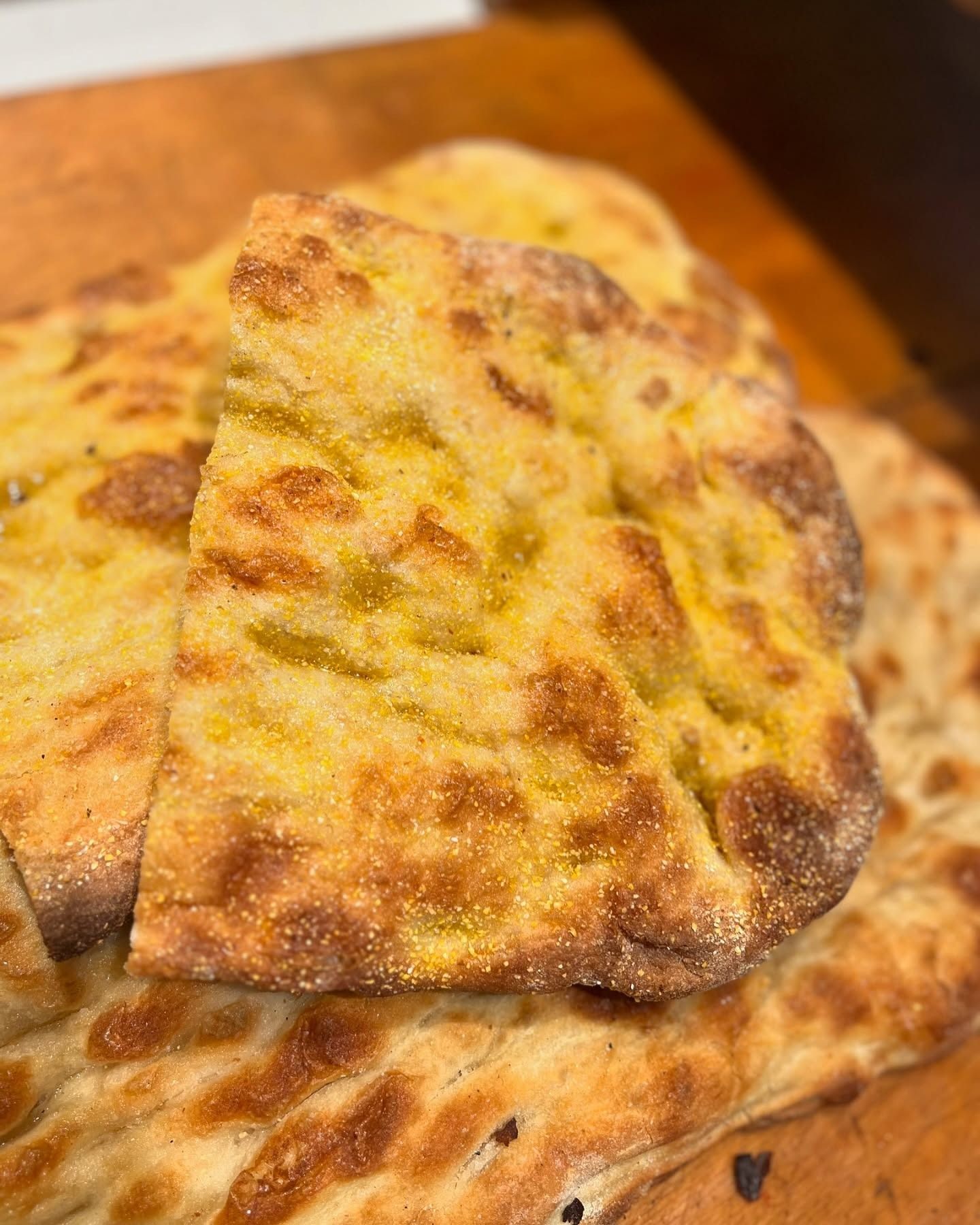Primo piano di una focaccia dorata. Un pezzo è tagliato e leggermente inclinato, mostrando una consistenza a fossette.