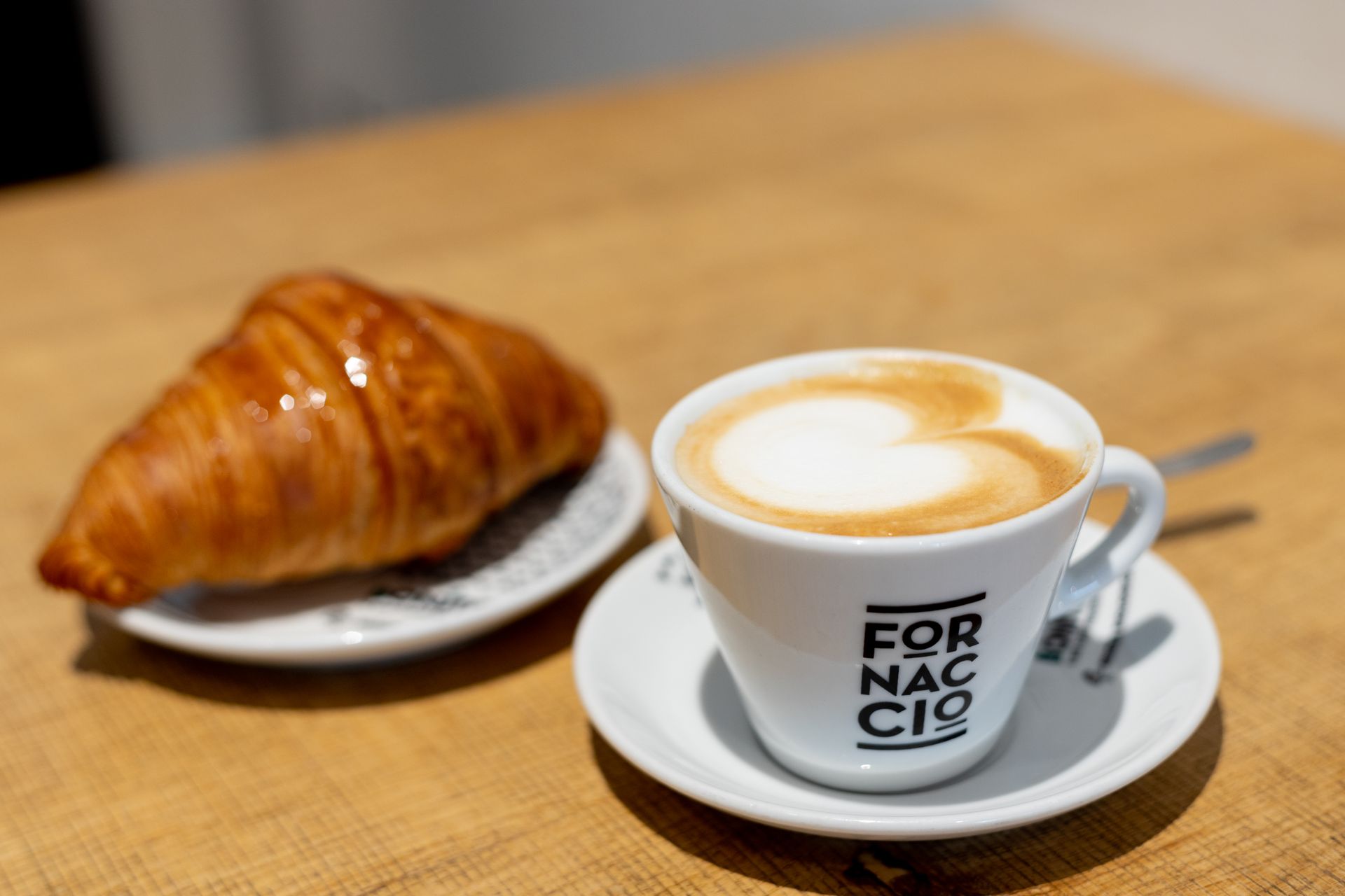 Cappuccino in una tazza bianca, croissant su un piattino, su un tavolo di legno.