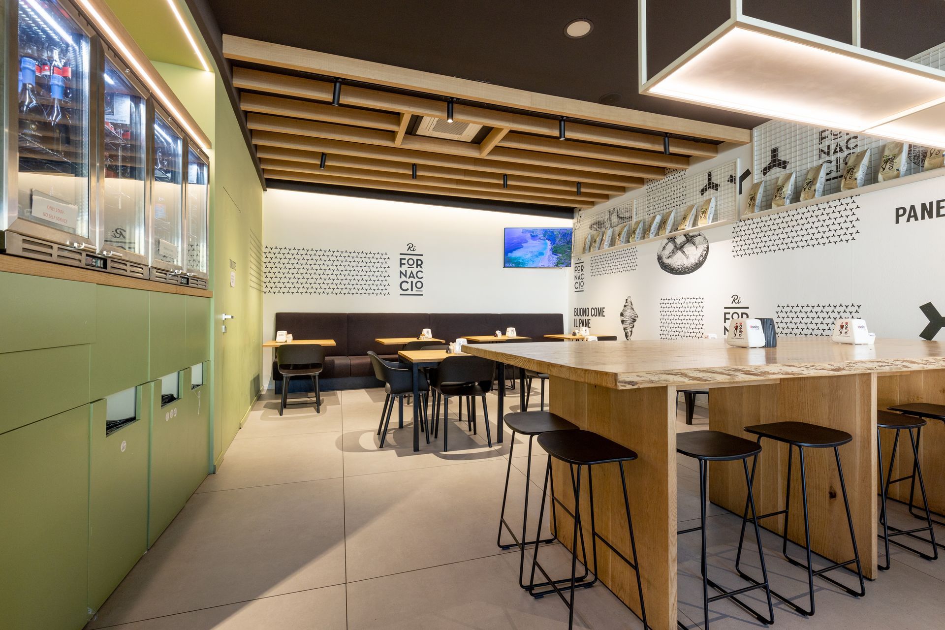 Interno di un ristorante moderno, con tavoli, sedie, sgabelli da bar e pareti decorate. Tonalità verde, nero e legno.