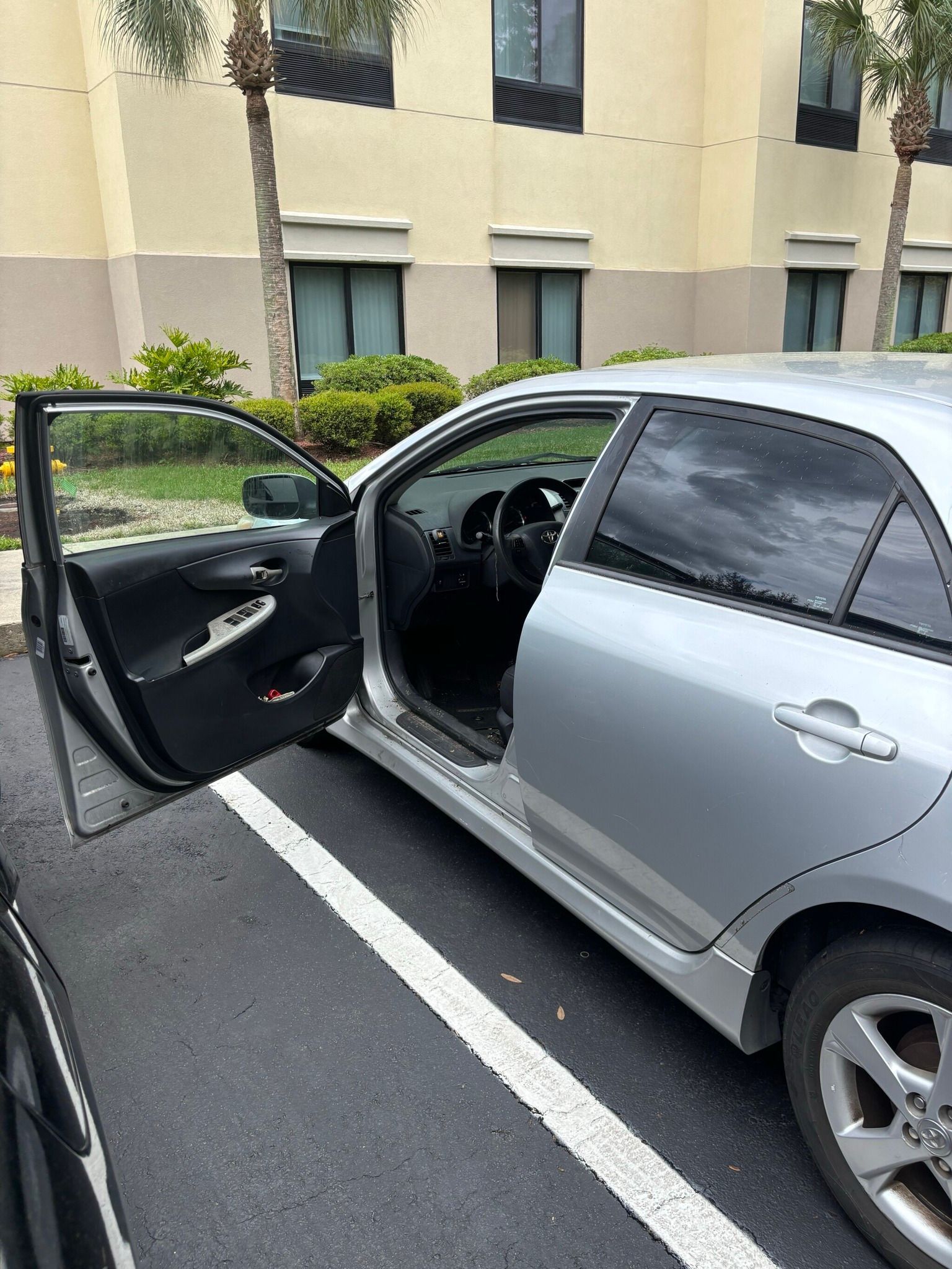 A silver car is parked in a parking lot with its doors open.