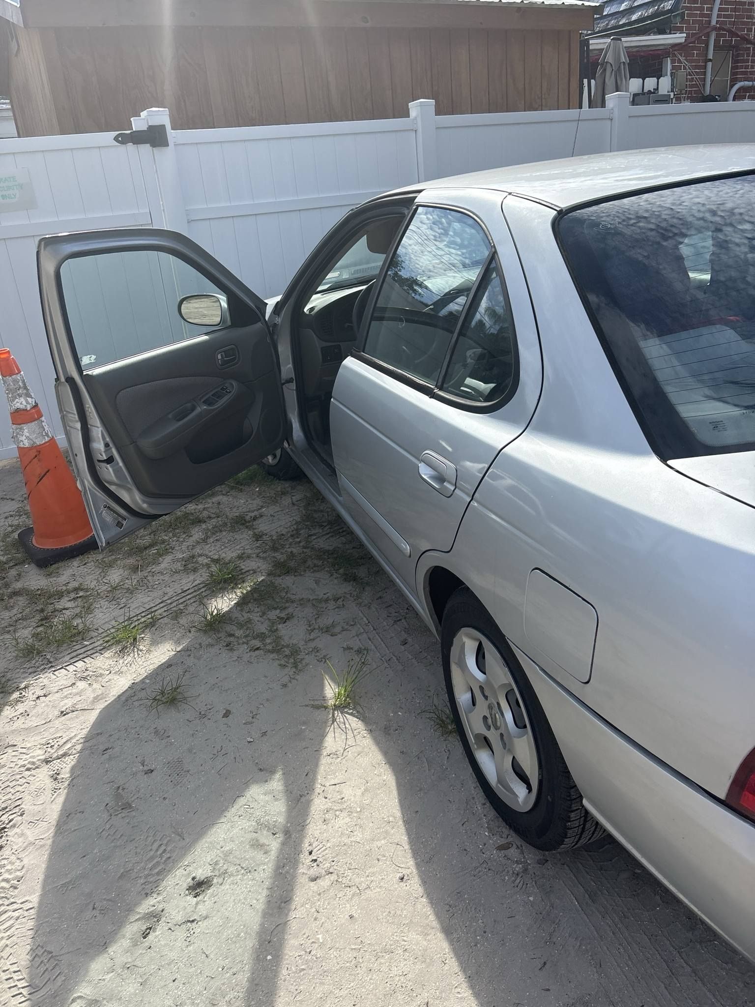 A silver car with its doors open is parked in front of a white fence.
