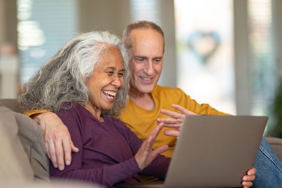 A couple happily waves at the computer screen during a video call at home.