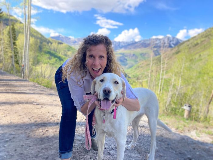 Erika, smiling, poses behind her cute dog, who appears to be smiling, too.