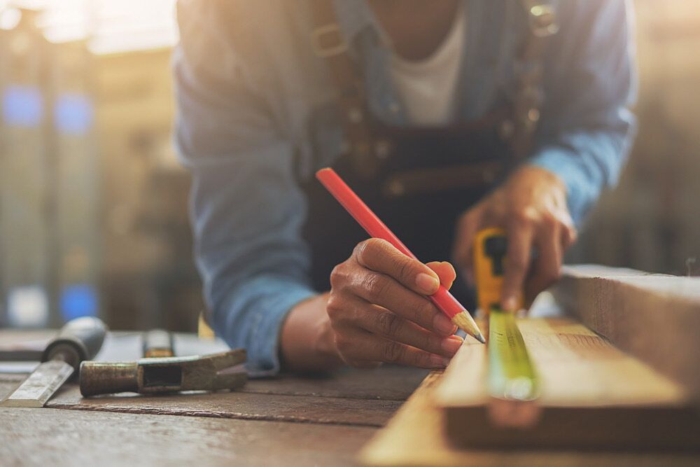 Carpenter Using a Tape Measure and Pencil to Mark Wood in a Workshop — Northco Constructions In Muirhead, NT