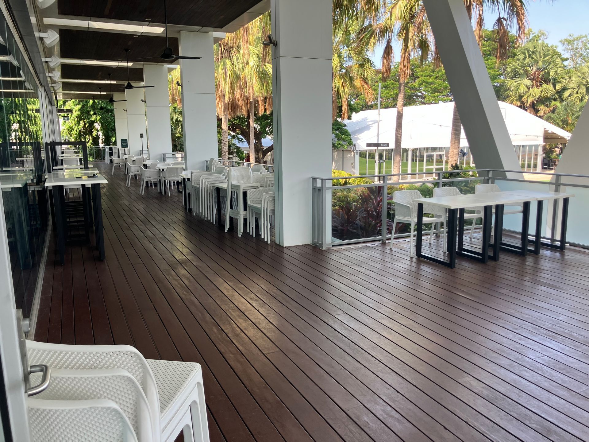 Outdoor Dining Area With Wooden Deck, White Tables and Chairs, Trees — Northco Constructions In Muirhead, NT