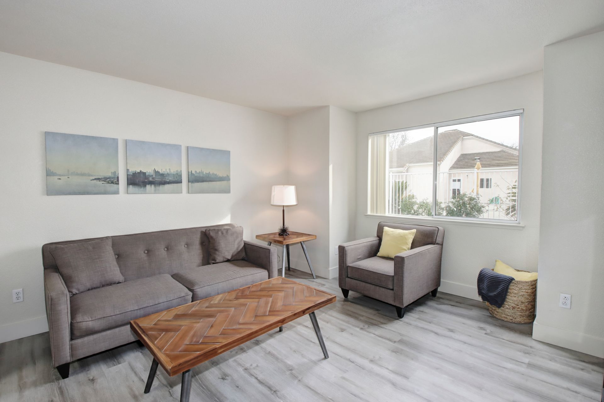 Living room with gray sofa, armchair, wooden table, art, and window.