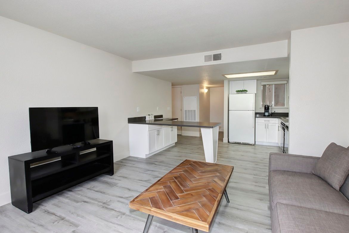 Living room with a TV, sofa, coffee table, and kitchen in the background.
