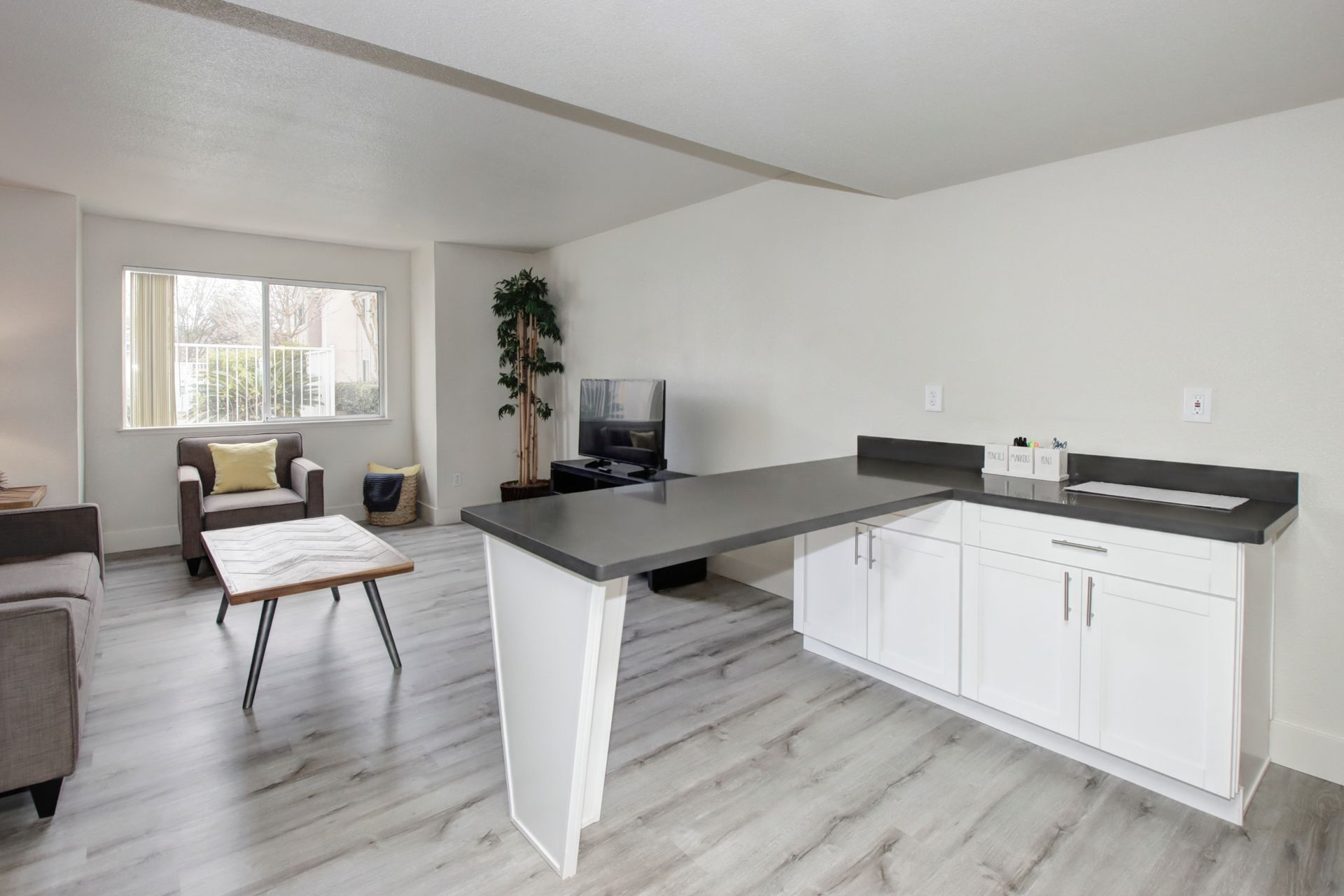 Living room with kitchen bar, white cabinets, wood-look flooring, and a window.