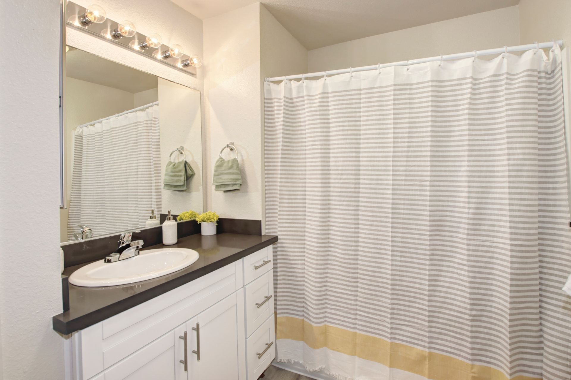 Bathroom with white vanity, dark countertop, white sink, striped shower curtain, and silver fixtures.
