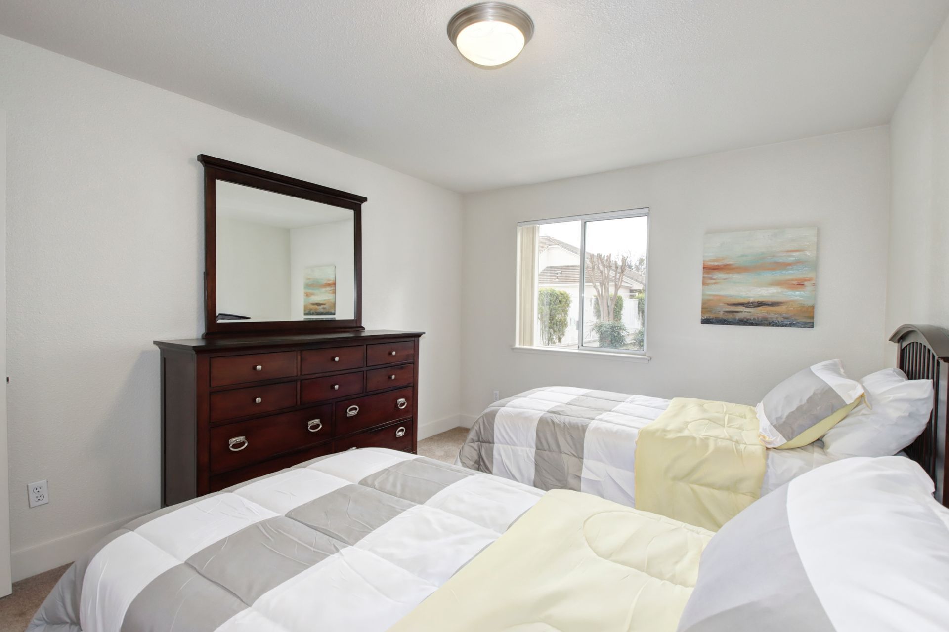 Bedroom with two beds, a dresser, and a window, all in a light-colored setting.