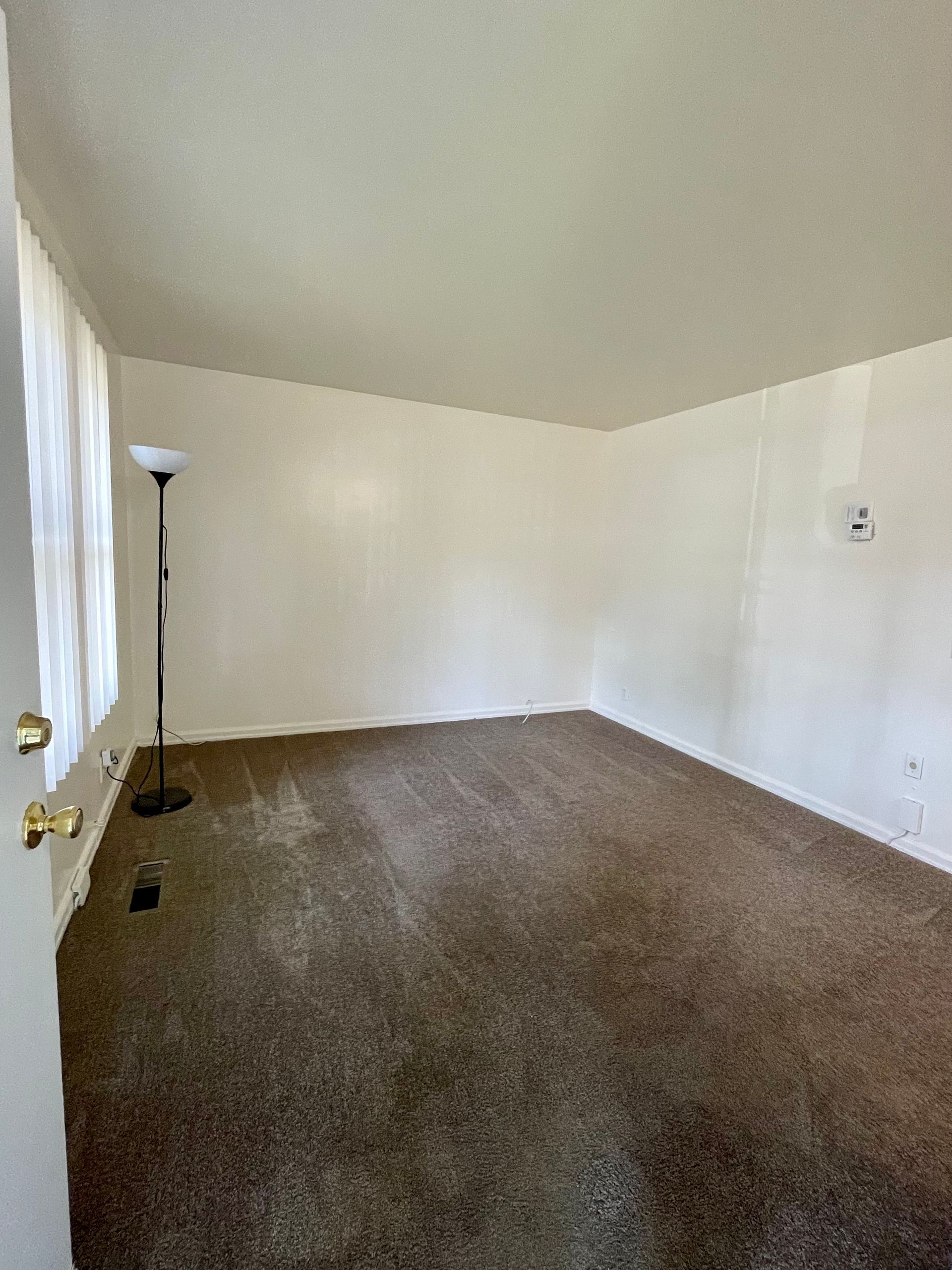 Empty room with stained brown carpet, white walls and a standing lamp.