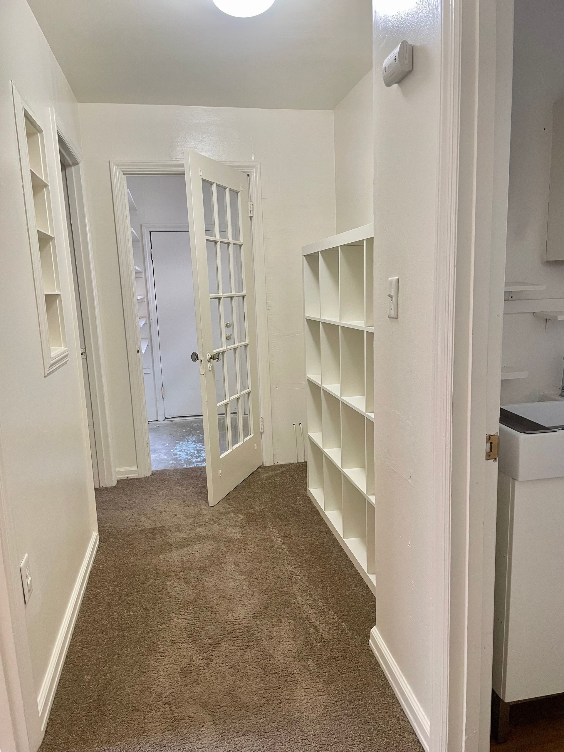 Narrow hallway with carpet, French doors, and built-in shelves.