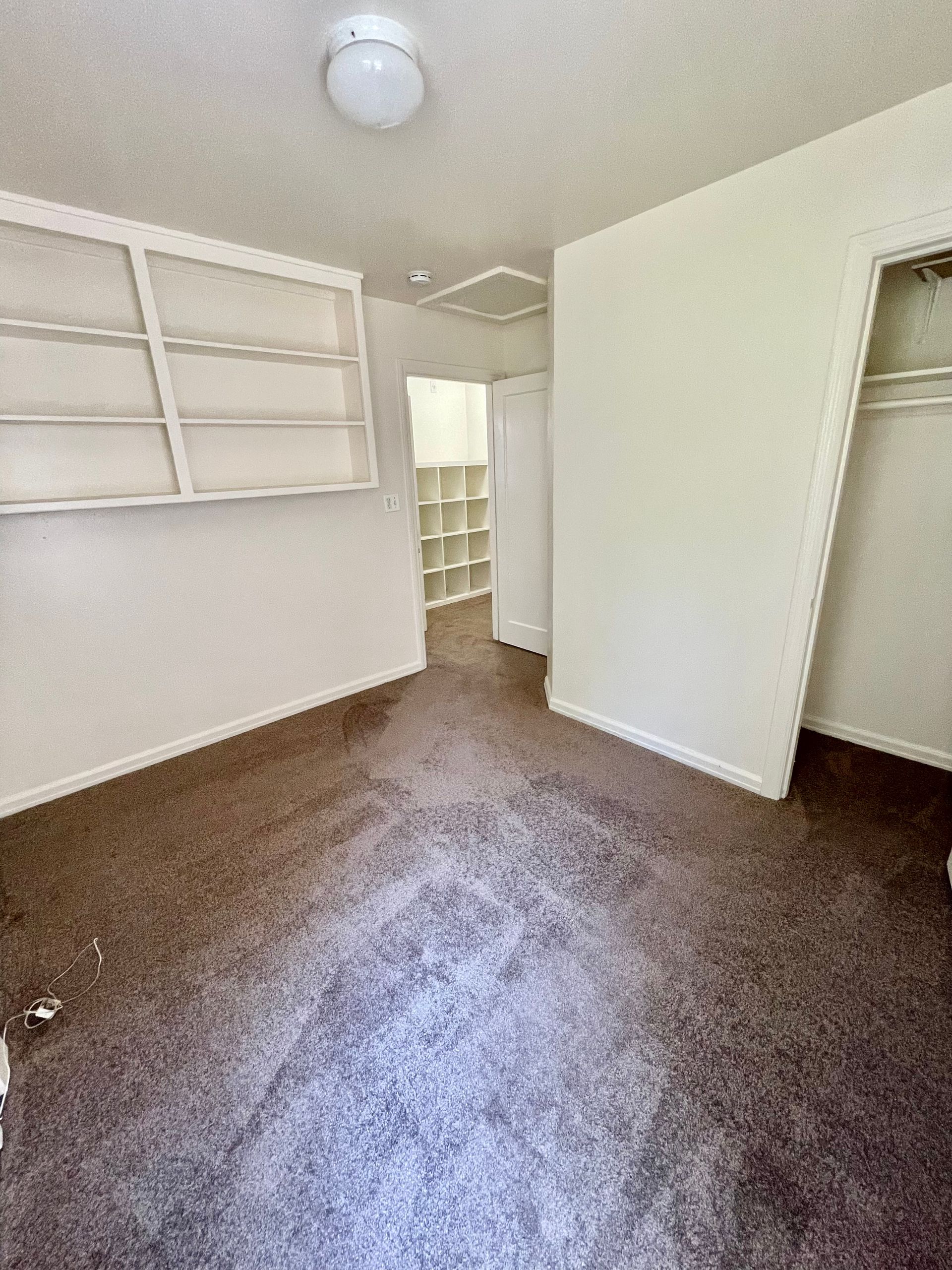 Empty room with brown carpet, built-in shelves, closet, and an entrance to another room.