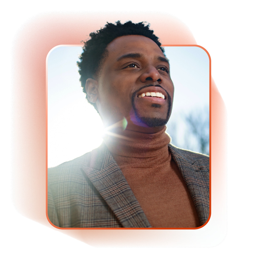 Daron K. Roberts in a rust-colored turtleneck and plaid blazer smiles, looking up at the sun.