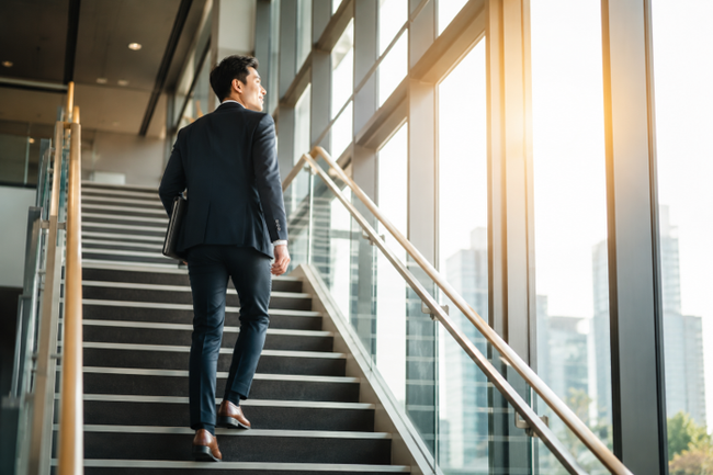 Businessman ascending a modern office staircase beside tall glass windows Businessman ascending a modern office staircase beside tall glass windows