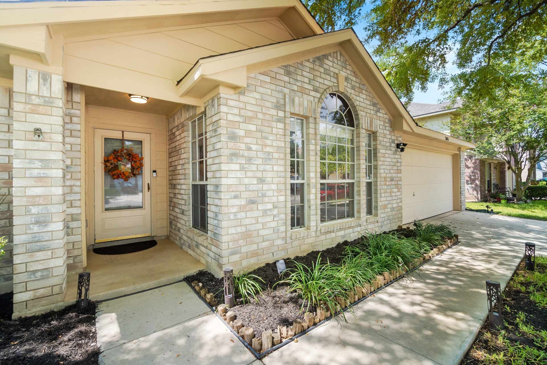 Brick house front porch with a decorated front door, arched window, and walkway along landscaping