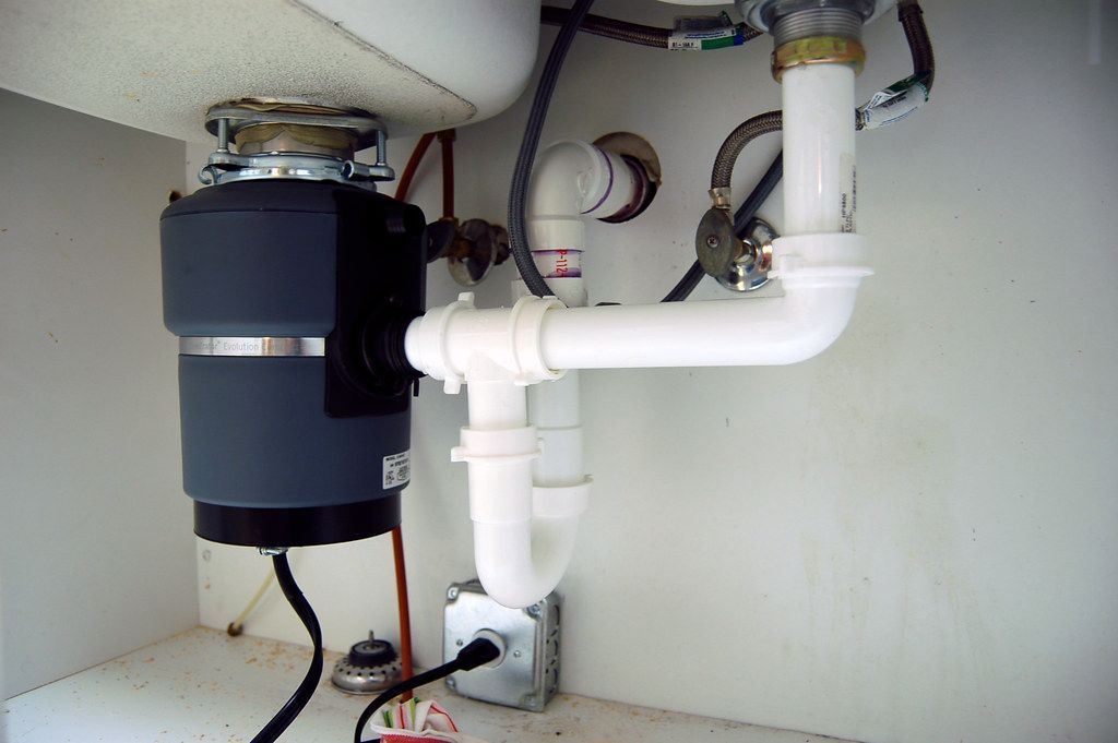 Blue garbage disposal connected to PVC pipe underneath a clean and tidy kitchen sink.