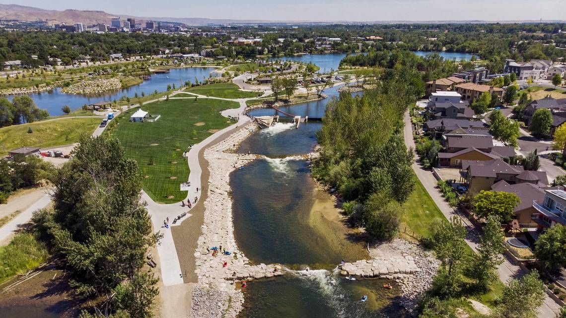 Aerial view of Boise River with artificial rapids, parkland, and buildings in the distance.