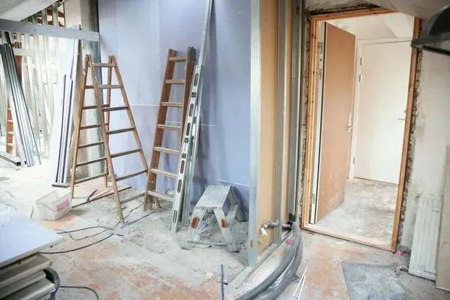 An A-frame ladder and an extension ladder are in a room that is being remodeled and ready for paint. The subfloor is not ready for flooring yet.