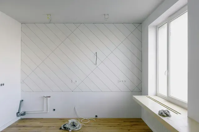 An empty all-white bedroom with a large window being prepped for paint, repairs, or upgrades.