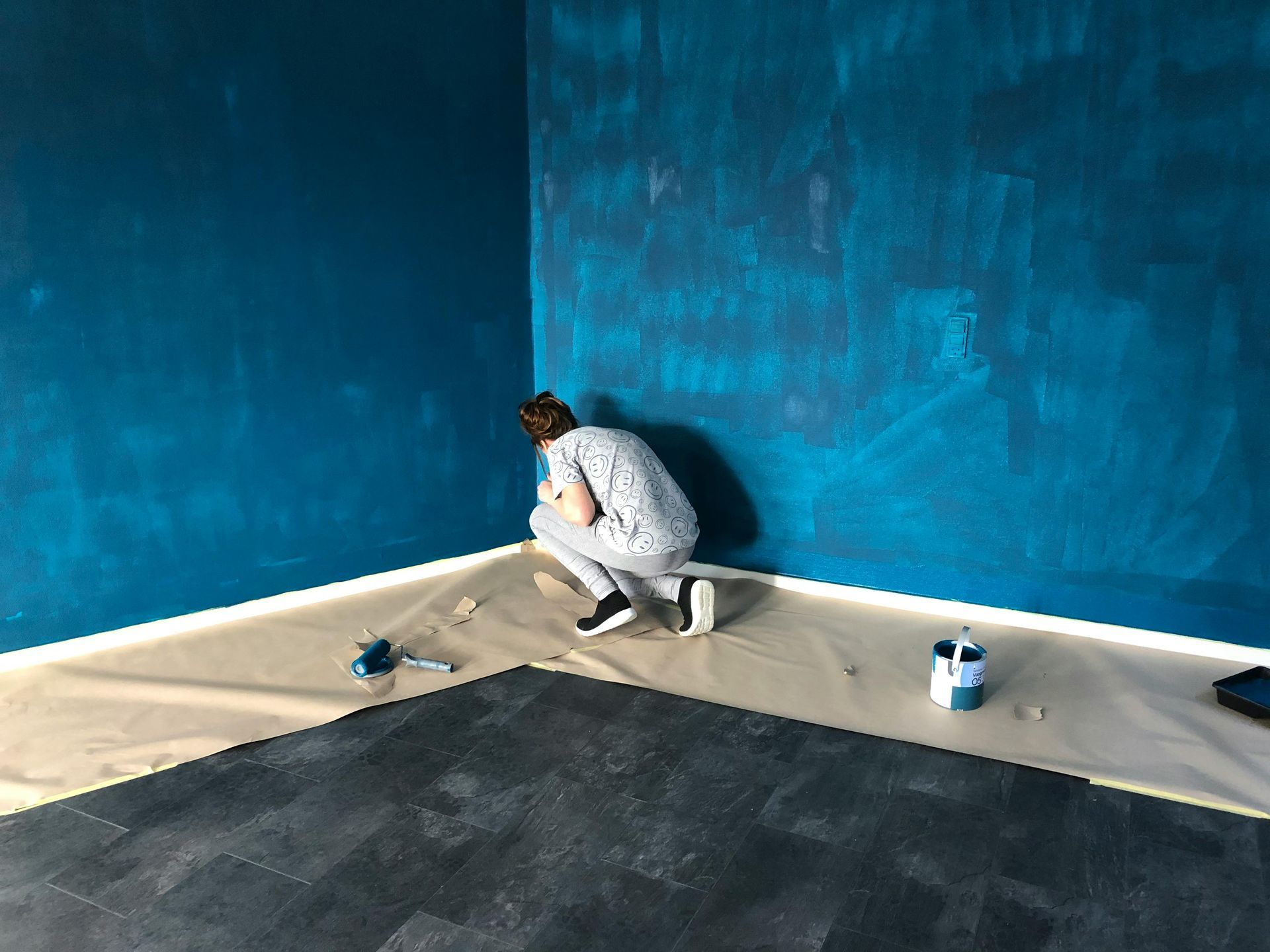 Man in white clothes painting the baseboards in an office.
