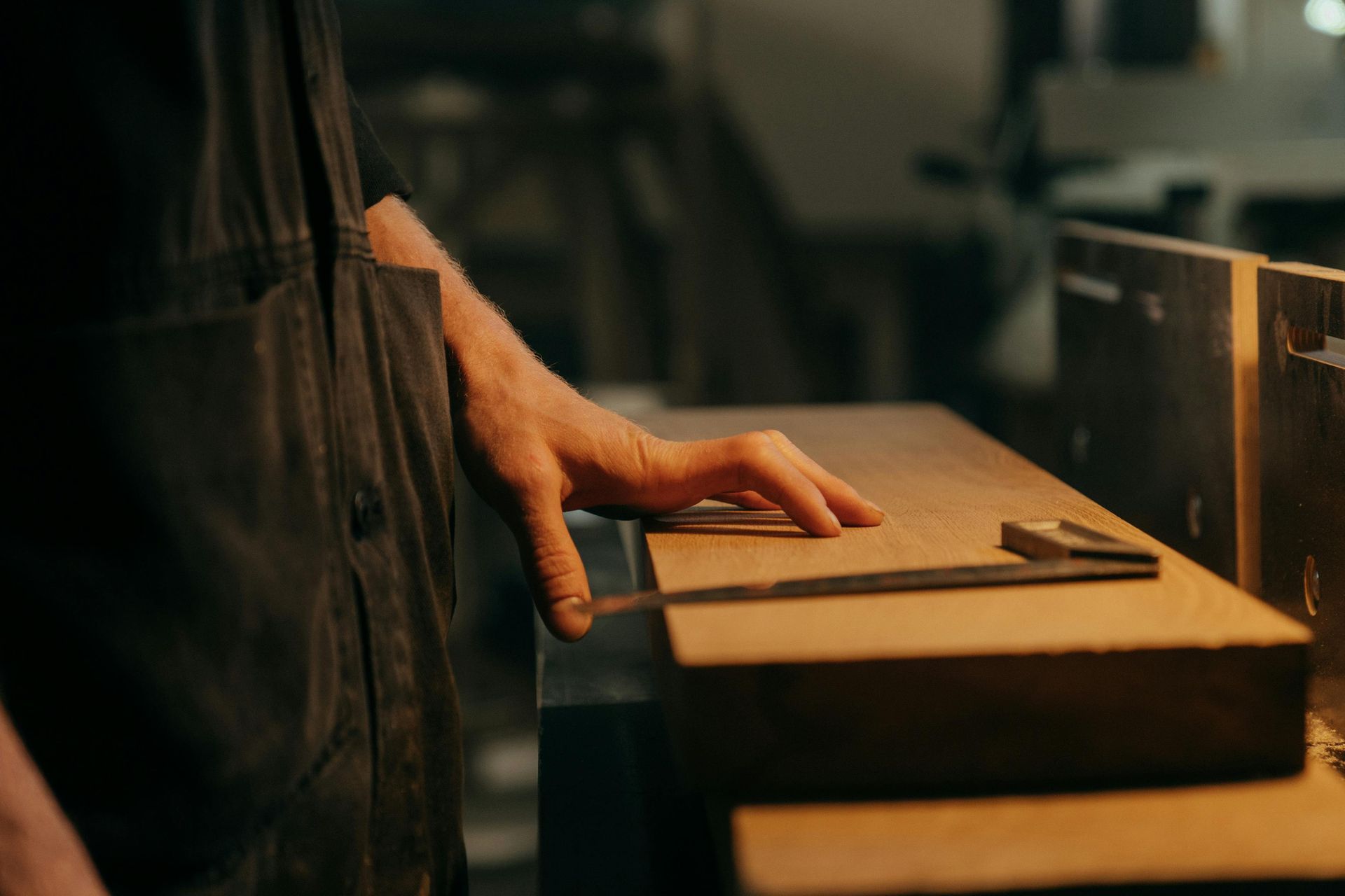 Person's hand using a caliper to measure a wooden plank in a workshop.