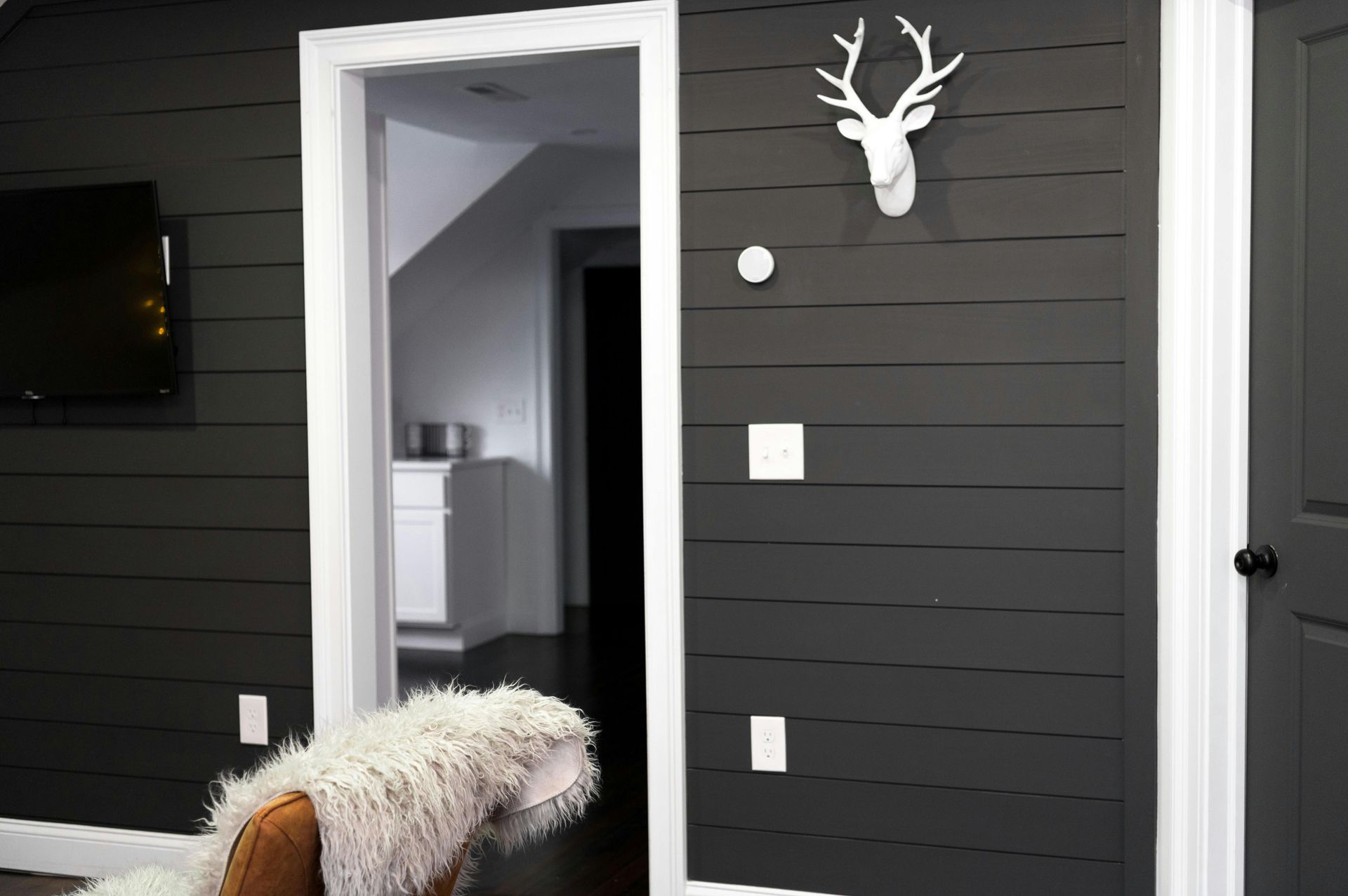 Living room with black shiplap and white moulding entering a kitchen.