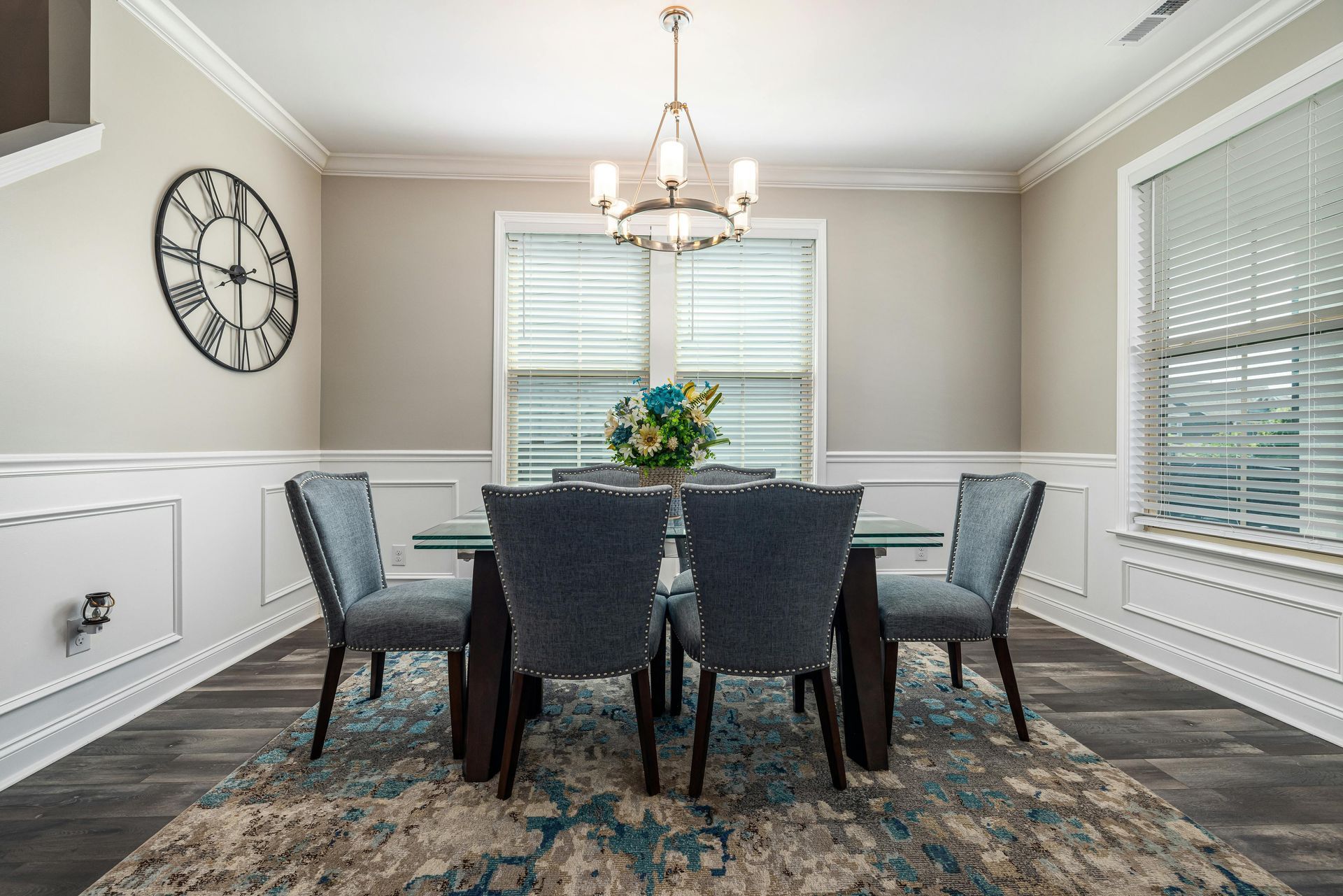 Dining room with 6 chair table, big windows, a Roman numeral Wall clock, and a classy chandelier.