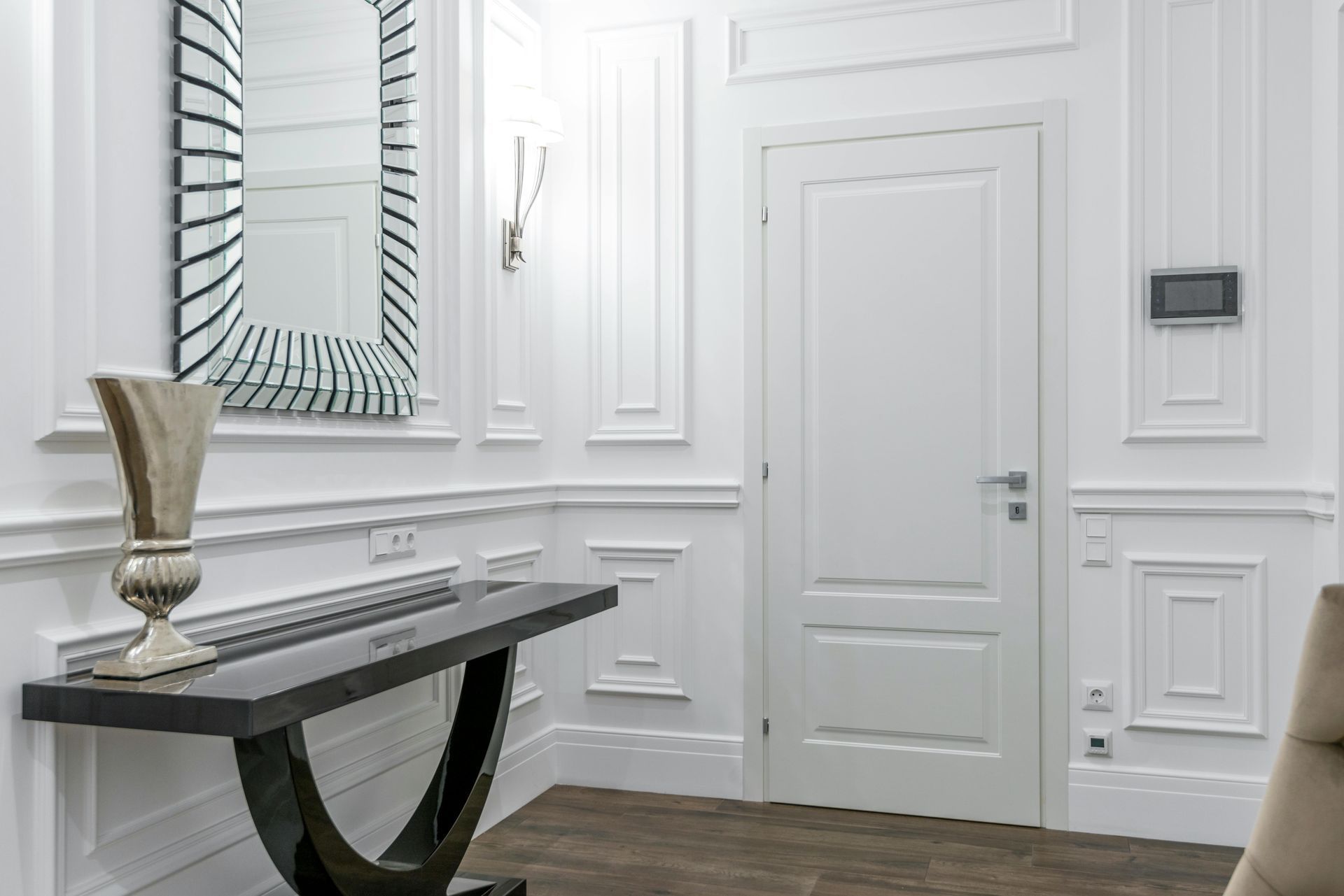 Entry way with all white walls, white wall paneling, moulding, and a big mirror over a brown entry room table.