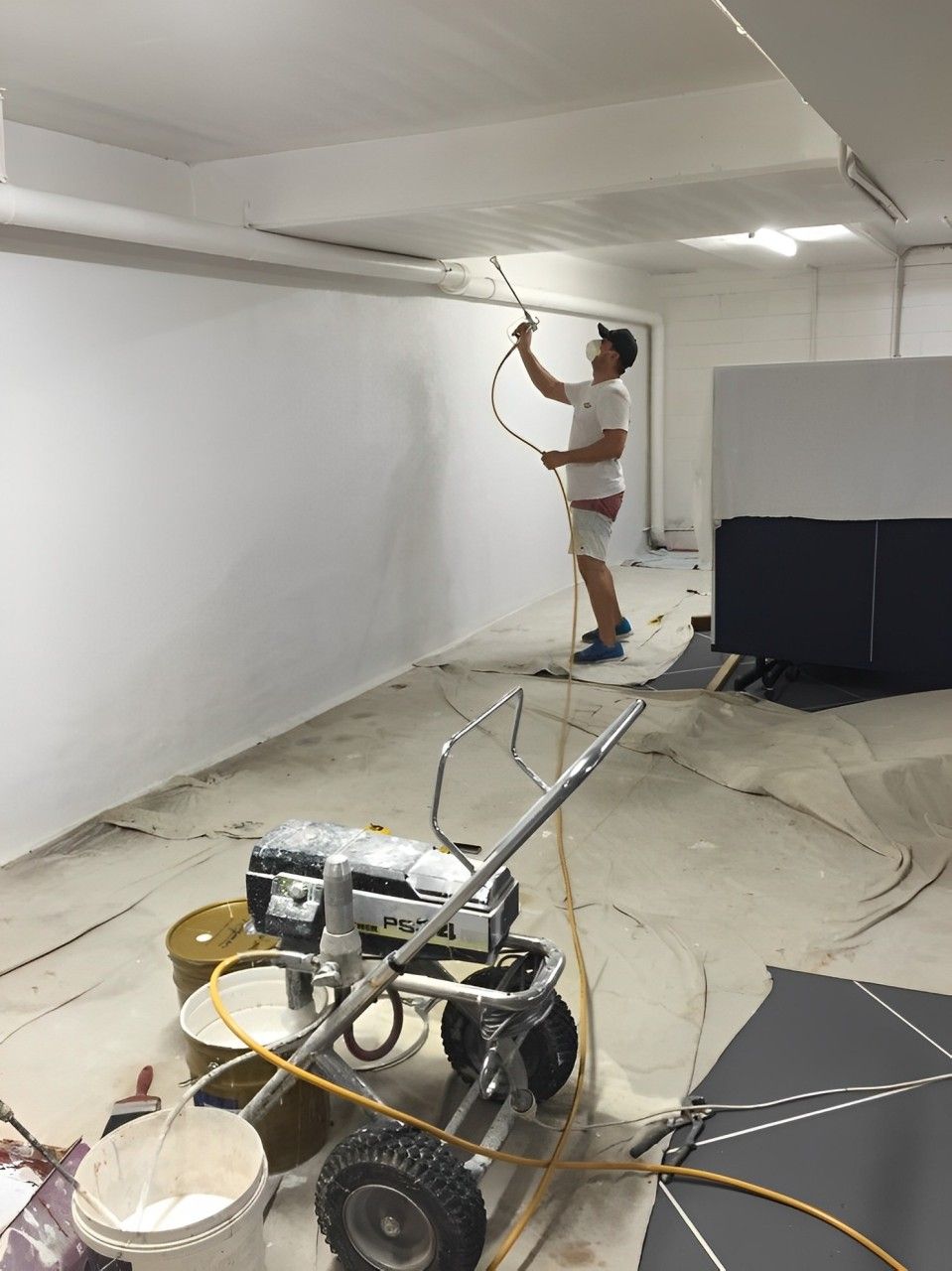 A Man Is Painting A Wall With A Sprayer In A Room — Tweed Heads Painting Service In Condong, NSW