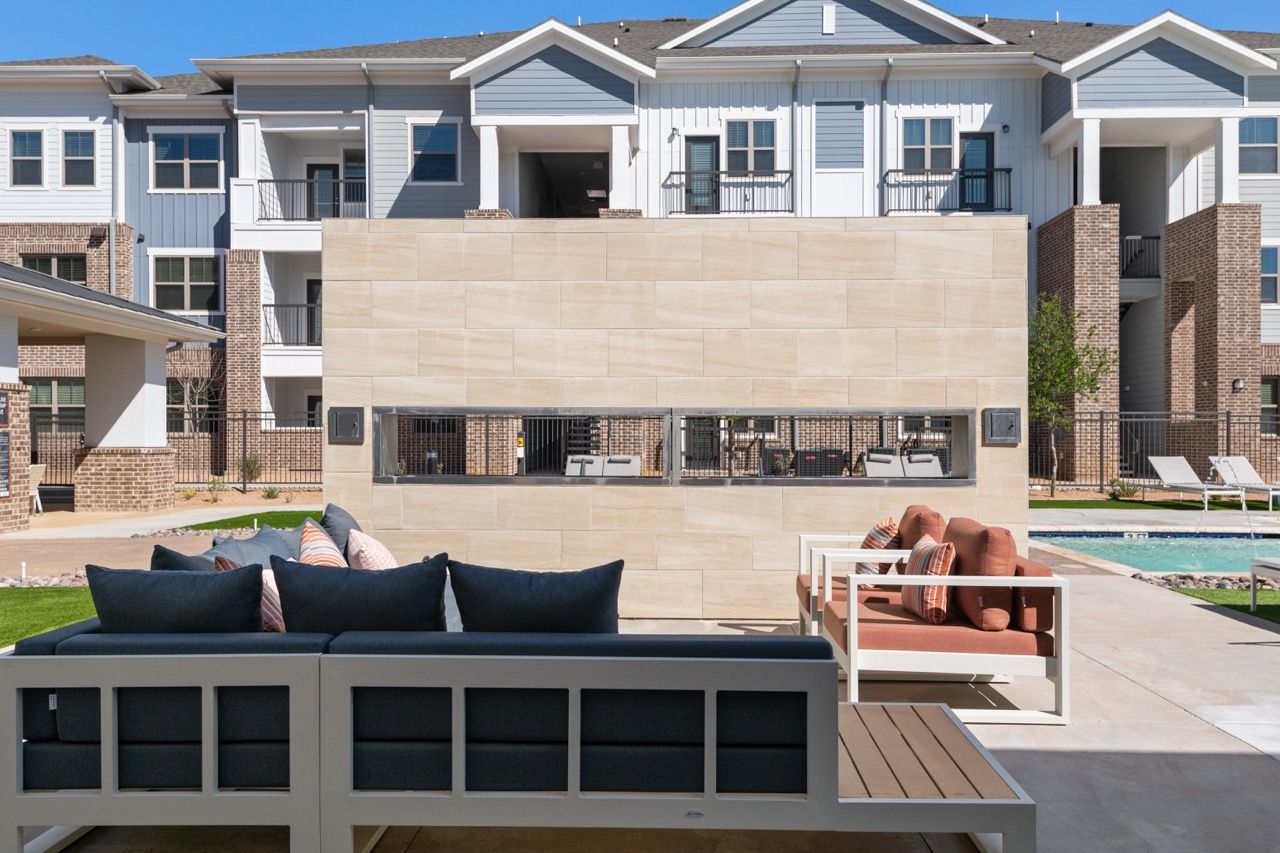 Outdoor communal lounge with seating, in front of modern apartment buildings and a pool.