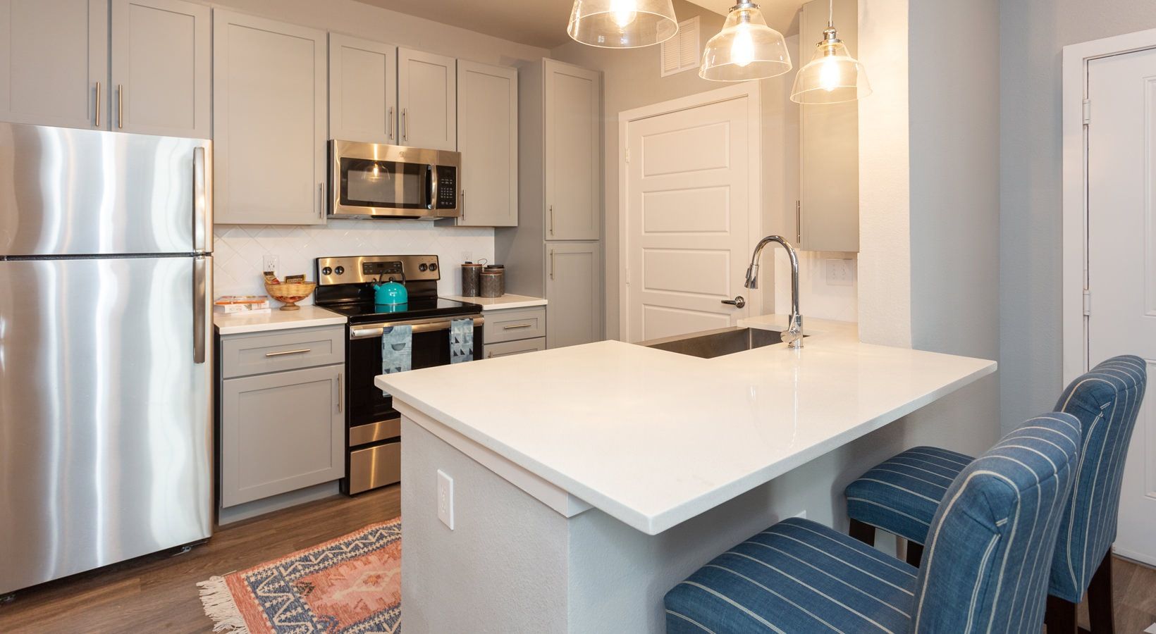 Modern kitchen with stainless steel fridge, range, microwave, and an island with a sink and blue striped stools.