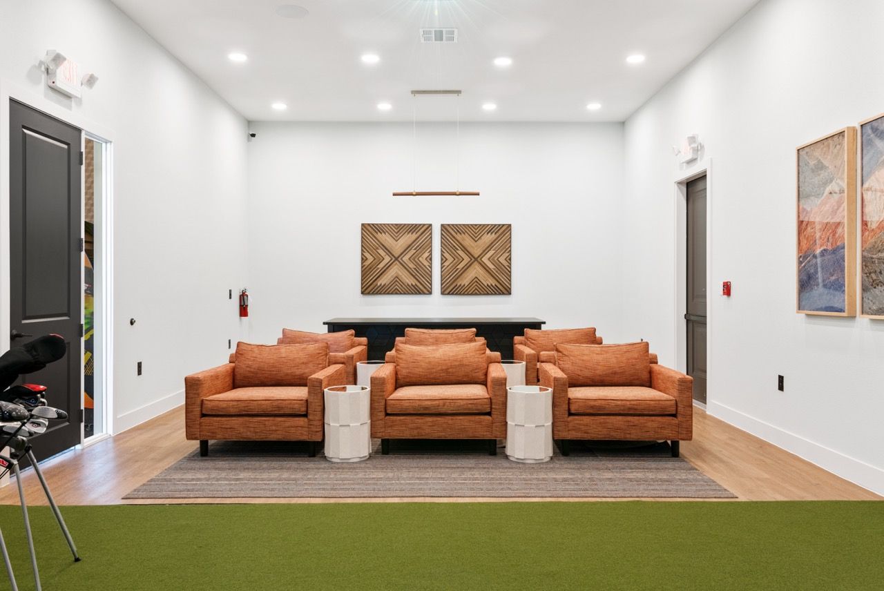 Bright communal lounge with orange armchairs, white walls, and abstract wall art.
