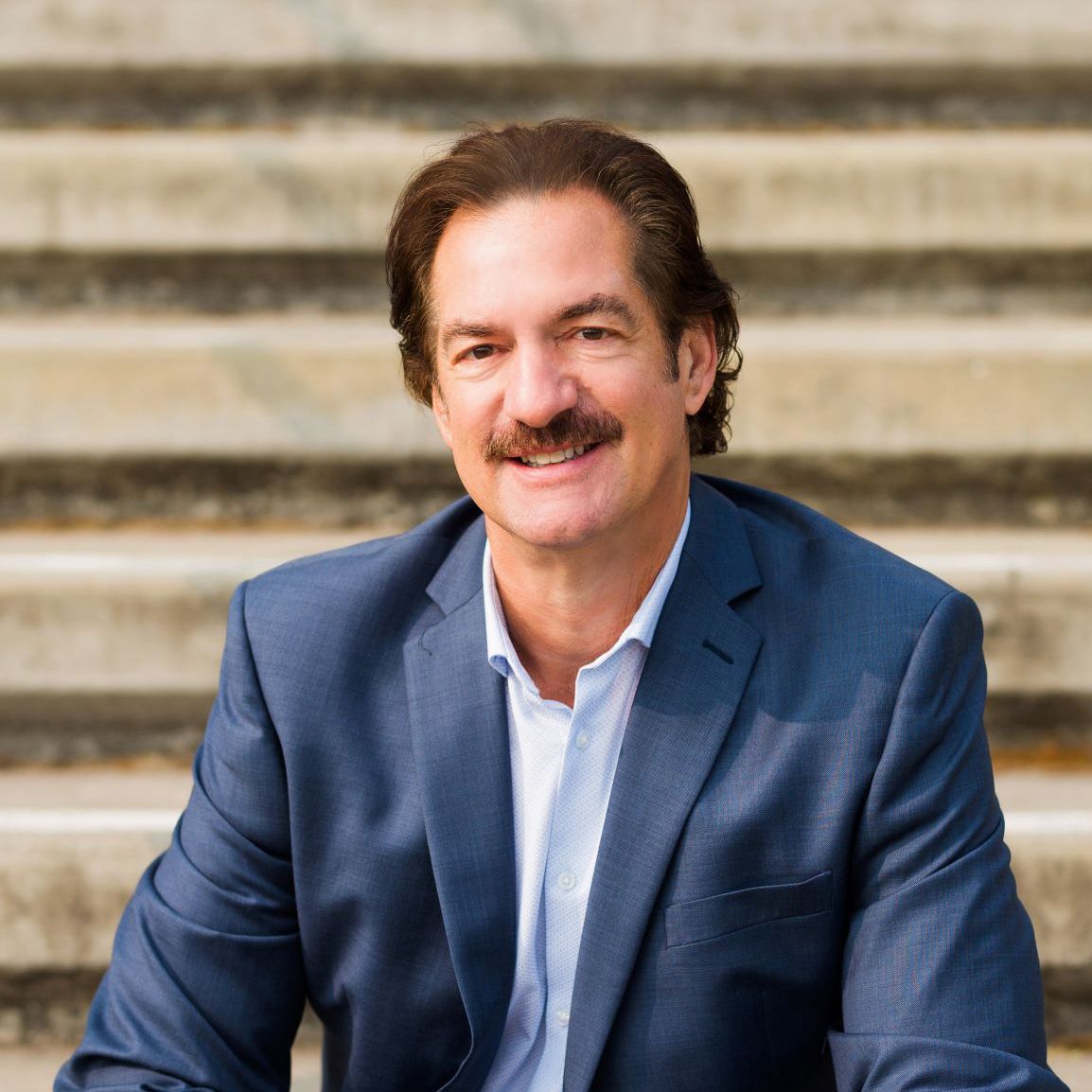 A man in a suit is sitting on a set of stairs and smiling.