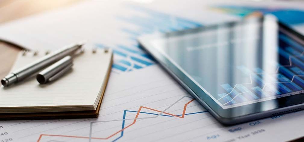 A tablet , a notebook , a pen , and a graph are on a table.