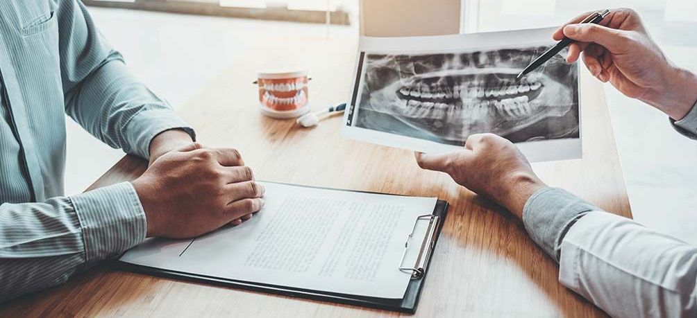 Two men are sitting at a table looking at an x-ray of their teeth.